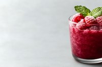 Fresh raspberry smoothie garnished with mint leaves and frozen berries in glass on light background. Healthy breakfast or dessert concept.