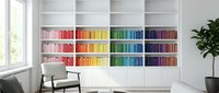 Modern home library with colorful rainbow organized books on white built-in shelves, minimalist reading corner with gray chair and plant in bright interior.