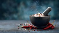 Stone mortar with mixed peppercorns and pestle surrounded by dried red chili peppers on dark background with copy space for food photography.