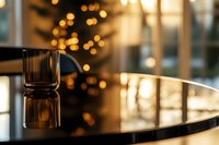 Empty glass on glossy black piano surface with soft bokeh lights and Christmas tree silhouette in background creating warm atmospheric holiday mood.