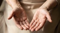 Open cupped hands of elderly person in warm lighting showing wrinkled skin and gentle gesture of giving or receiving help in caring supportive moment.