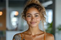 Young mixed-race woman with curly blonde hair and rose tattoo smiling warmly in modern office space for lifestyle and business content.