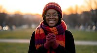 Happy young African American woman wearing knit hat and colorful scarf smiling outdoors during golden hour sunset in park for lifestyle content.
