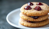 Fresh baked cranberry sugar cookies stacked on white plate with selective focus, showing crispy texture and glistening berries in natural light.