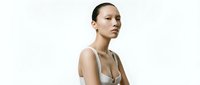 Young woman with East Asian ethnicity, sleek pulled-back hair, wearing neutral beige tank top, isolated on white background for skincare, wellness, and beauty product marketing campaigns.
