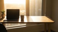 Laptop and coffee cup on wooden desk by window with natural light, workspace setup for remote work and productivity.