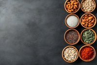 Wooden bowls with healthy superfoods, nuts, seeds, and spices arranged on dark stone background with copy space for text. Great for food blogs and recipes.