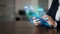 Businessman using smartphone with holographic financial data charts and graphs floating above device for mobile banking and investment analysis.