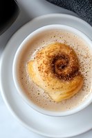 Fresh baked cinnamon roll with brown sugar and spices sprinkled on top served on white ceramic plate, close up view with selective focus.