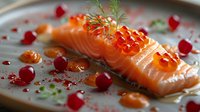 Fresh salmon fillet topped with red caviar, dill garnish and pomegranate seeds on gray plate, elegant restaurant presentation with sauce drops and herbs.
