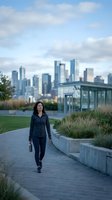Professional Asian businesswoman walking on urban park pathway with city skyline background during evening hours for corporate lifestyle concepts.