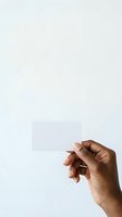 Male hand with medium-dark skin tone holding blank white card against neutral background. Isolated on white for business card mockups, branding presentations, and marketing materials.