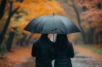 Silhouette of couple sharing umbrella while walking in autumn park. Orange fall foliage creates romantic mood as they stroll along wet path in rain.