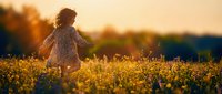 Young girl with light skin tone and long hair running through golden wildflower field at sunset, wearing floral dress, enjoying nature and outdoor freedom during golden hour.