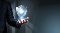 Businessman in dark suit holding glowing security shield symbol representing cybersecurity protection and data safety in corporate environment.