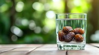 Fresh dates soaking in clear water glass against blurred green natural background, healthy organic snack for breaking fast during Ramadan season.