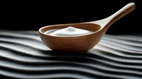 Wooden spoon with white salt or sugar powder on black textured wavy background, dramatic lighting creates contrast between light and shadow in minimalist style.