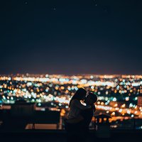 Romantic couple silhouette kissing on rooftop terrace overlooking blurred city lights at night creating intimate urban atmosphere for dating concepts.