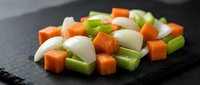Fresh diced vegetables including carrots, celery and onions arranged on dark slate surface for cooking preparation and culinary ingredients display.