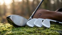 Golf clubs on green grass with warm sunlight creating bokeh background for sports equipment and recreational activity concepts.