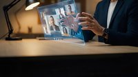 Businessman in dark suit holding transparent digital tablet displaying video conference with multiple participants and data analytics interface.