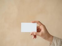 Hand holding blank white business card against neutral beige background, suitable for branding, corporate identity, and marketing mockup designs.