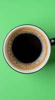Fresh black coffee in white ceramic cup with creamy foam ring on bright green background, viewed from above. Minimalist food photography for cafe menus and blogs.