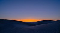 Desert sand dunes at sunset with golden orange sky transitioning to deep blue twilight, creating serene landscape for travel and nature backgrounds.