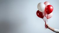 Hand holding festive balloons in red, pink and white colors against light gray background, minimalist celebration concept for greeting cards and banners.