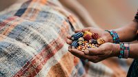 Farmer's hands holding harvested grains and seeds over traditional woven textile, showcasing agricultural produce and rural farming practices for harvest and sustainability themes.