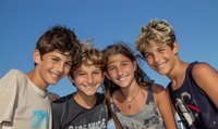 Group of happy diverse teenagers smiling outdoors against blue sky background, representing friendship, youth culture and summer activities.