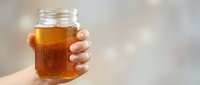 Person holding glass jar filled with amber liquid, ideal for beverage, food and drink marketing materials.