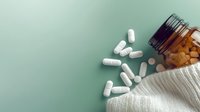 White capsule pills scattered from brown glass bottle on mint green background with knitted fabric texture, healthcare and medicine concept.
