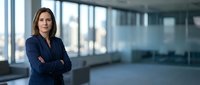 Confident businesswoman with crossed arms in modern office space with large windows and city view background for corporate presentations.