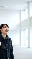 Young East Asian woman wearing dark denim jacket in bright, minimalist interior space with large windows and natural light, suitable for lifestyle, business, and commercial projects.