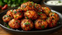 Spicy glazed meatballs garnished with fresh herbs on black plate, served with creamy dipping sauce, close up view on rustic wooden table background.