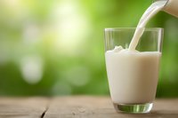 Fresh milk pouring into clear glass on wooden table with green natural bokeh background, creating splash and dynamic flow. Suitable for dairy advertising.