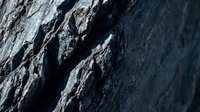 Dark gray rock surface with deep cracks and rough textured stone formation showing natural weathering patterns and geological layers for backgrounds.