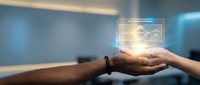 Hands holding glowing digital hologram with data analytics interface in modern office environment, representing technology innovation and business intelligence solutions.