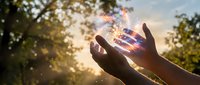 Hands reaching toward glowing magical light with sparkles and energy rays during golden hour sunset, spiritual awakening and manifestation concept.