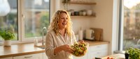 Happy blonde woman holding fresh salad bowl in bright modern kitchen with natural lighting and wooden countertops for healthy lifestyle content.