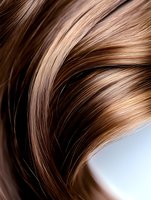 Flowing strands of glossy brown hair with honey highlights against light background, showcasing natural movement and healthy shine for beauty and haircare advertising.