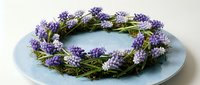 Handmade spring wreath with purple muscari grape hyacinth flowers and green foliage arranged in circular design on light blue plate for home decor and crafting.