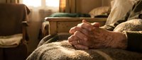 Close-up of elderly person's wrinkled hands resting on lap in warm sunlit room, conveying comfort, aging, and peaceful moments at home.
