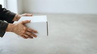Person with medium skin tone holding white box on concrete surface, suitable for delivery, shipping, unboxing, and e-commerce concepts.
