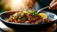 Steaming hot beef goulash with mushrooms and vegetables in cast iron pan, garnished with fresh herbs and lemon. Traditional homestyle dish with rich sauce.