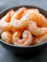 Fresh peeled shrimp in black ceramic bowl, close up view of cooked pink prawns. Macro food photography with selective focus for restaurant menus.