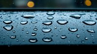 Macro shot of water droplets on dark metallic surface with bokeh lights in background creating atmospheric rainy mood. Natural condensation pattern.