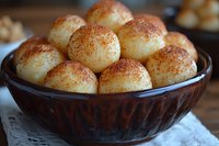 Homemade sweet dumplings dusted with cinnamon in brown ceramic bowl, close-up view showing soft texture and golden-brown coating on traditional dessert.