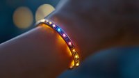 Glowing LED bracelet with multicolored lights creating magical bokeh effect against dark background, close-up view shows modern wearable technology.